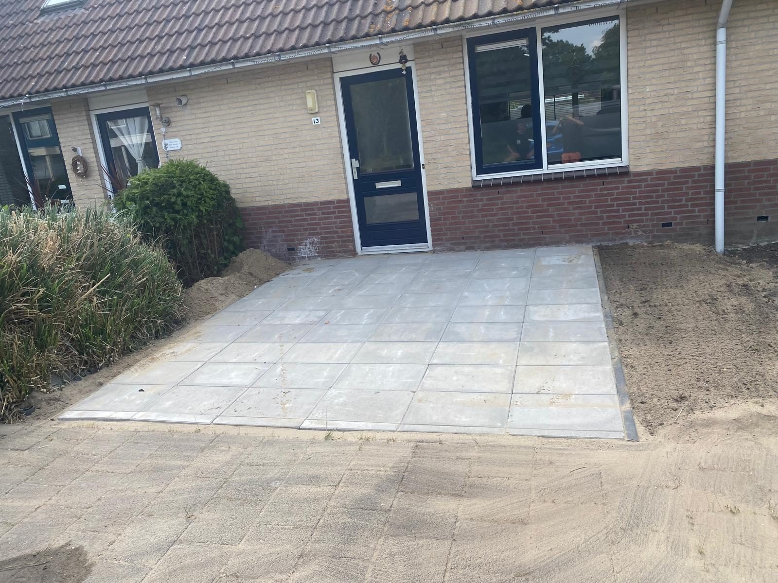 Nieuw terras van lichte tegels aan de voorzijde van een woning